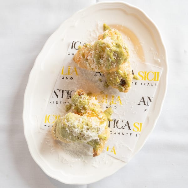 Antica Sicilia's fried dough with green sauce and grated cheese, served on a white plate with branded paper.