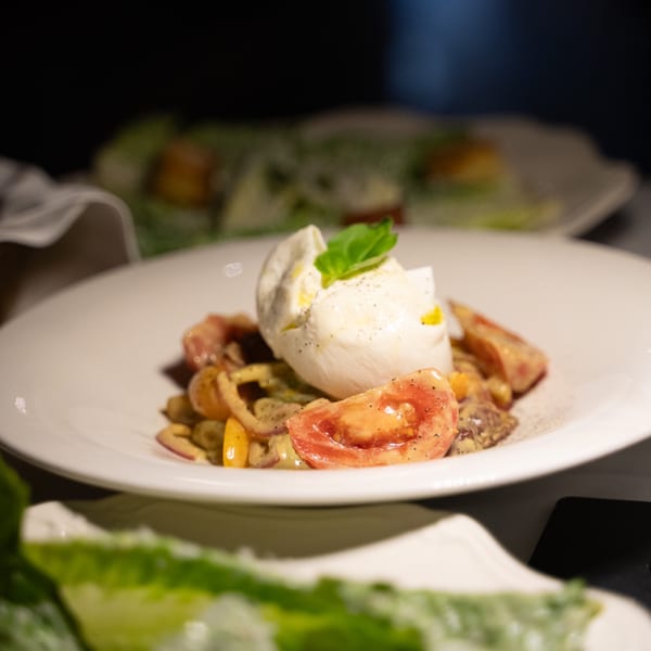 Antica Sicilia's pasta dish with burrata, fresh tomatoes, and basil on a white plate.