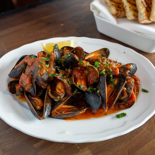 Antica Sicilia's mussels in red sauce with parsley and a lemon wedge, served with toasted bread.