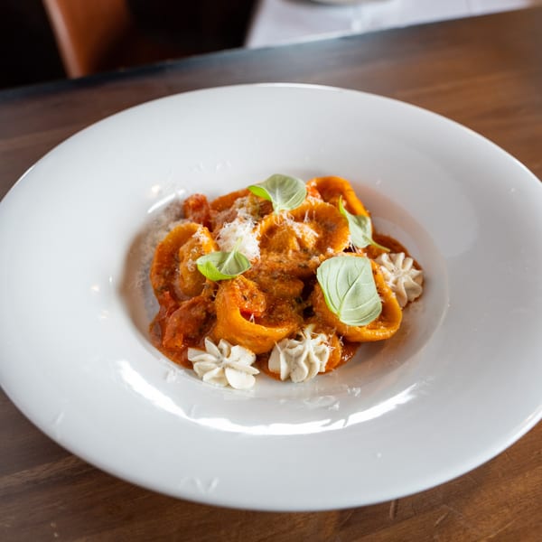 Antica Sicilia's tortelloni pasta in red sauce, garnished with basil and cream dollops.