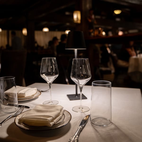 A set table at Antica Sicilia with wine glasses, plates, and a small lamp in a dimly lit dining room.