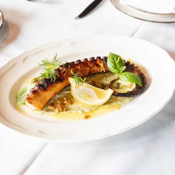 Grilled octopus with lemon, basil, pine nuts, and capers on a bed of green sauce.