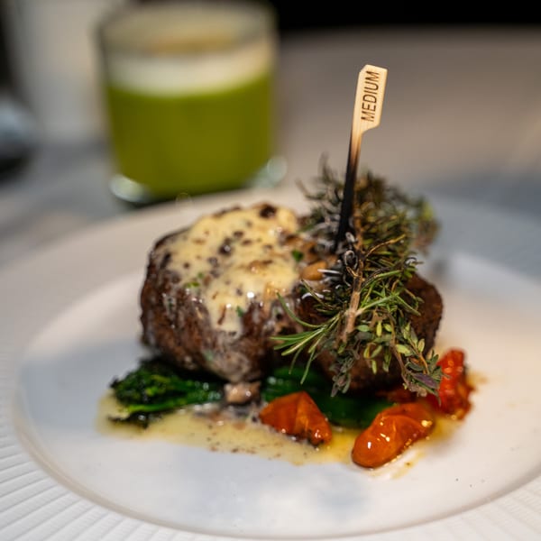 Antica Sicilia's medium-cooked steak with sauce, herbs, roasted tomatoes, and greens on a white plate.